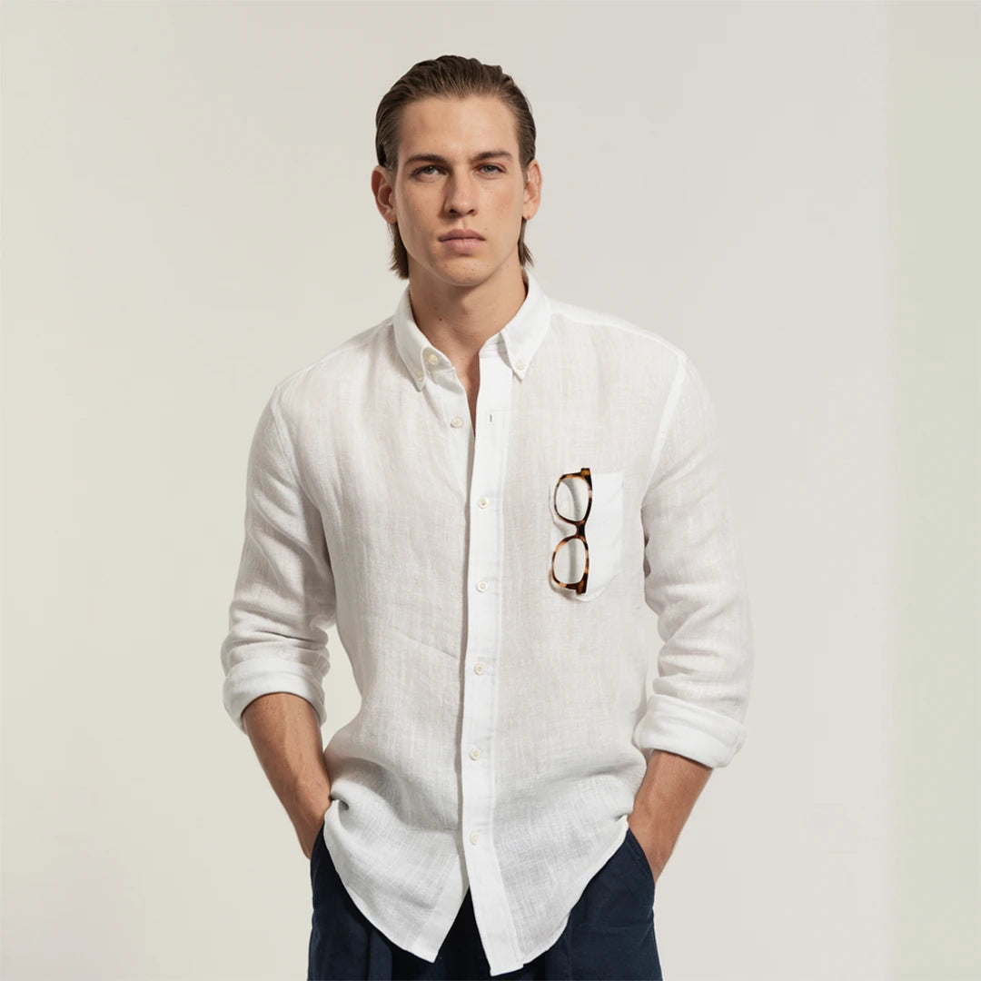 A man wearing a white linen shirt with a classic spread collar and mother-of-pearl buttons, paired with dark trousers.