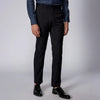 A man standing wearing black Kensington trousers with a mid-rise waist and sharp pleats, paired with a shirt and shoes.