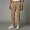 A man standing wearing brown Kensington trousers with a mid-rise waist and sharp pleats, paired with a shirt and shoes.