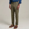 A man standing wearing olive Kensington trousers with a mid-rise waist and sharp pleats, paired with a shirt and shoes.