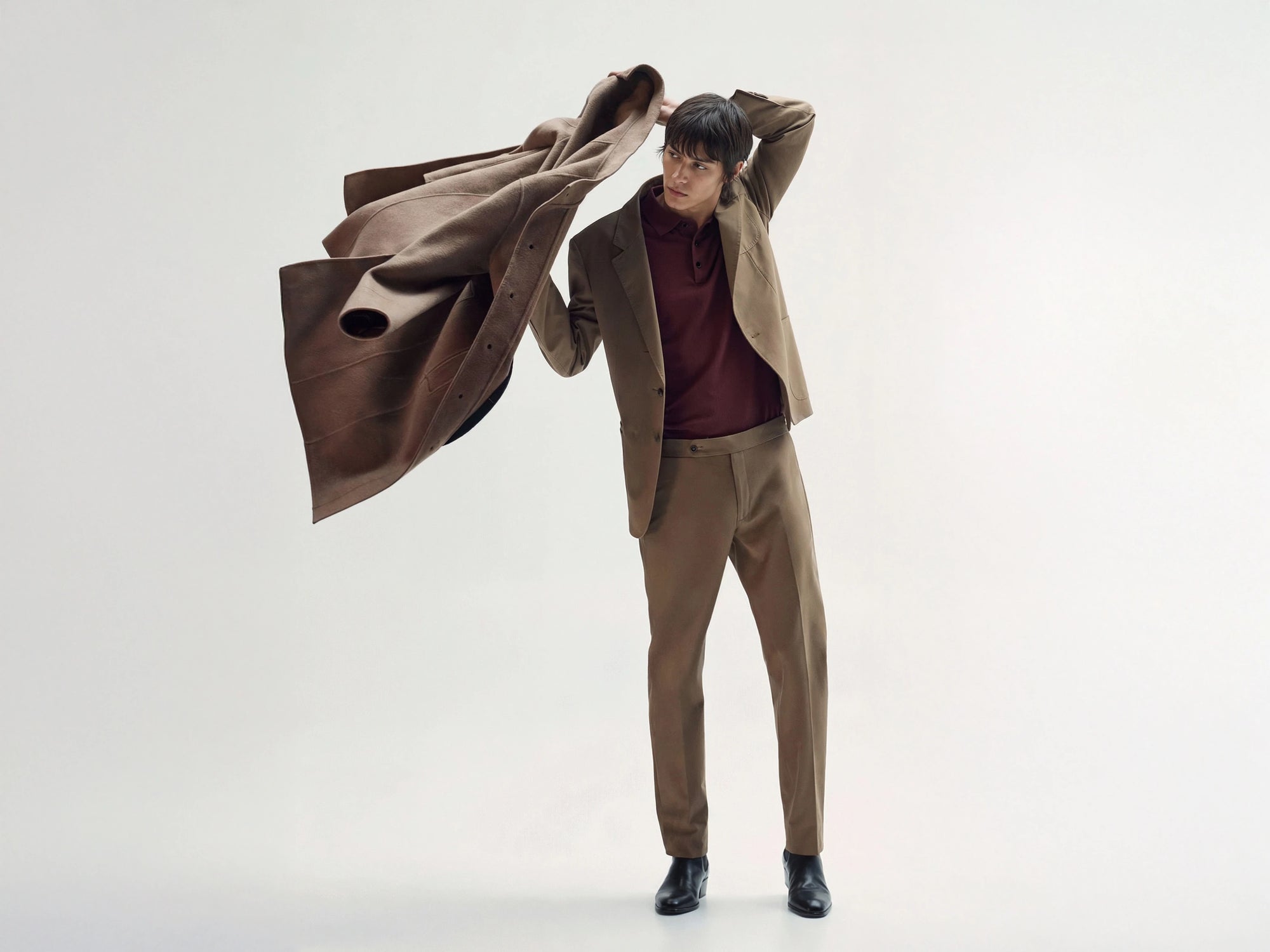 Man holding a brown coat over his shoulders against a white background