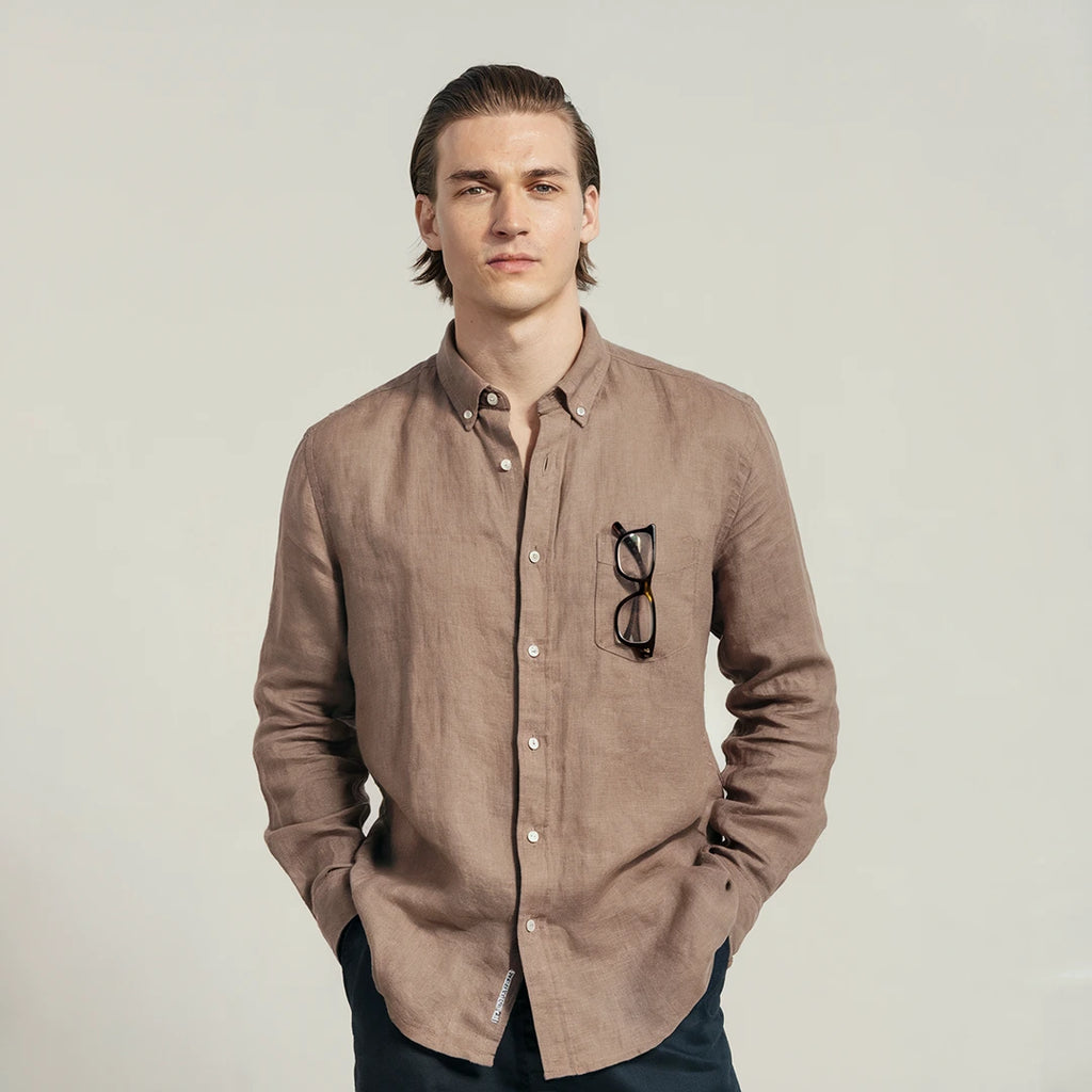 A man wearing a brown linen shirt with a classic spread collar and mother-of-pearl buttons, paired with dark trousers.
