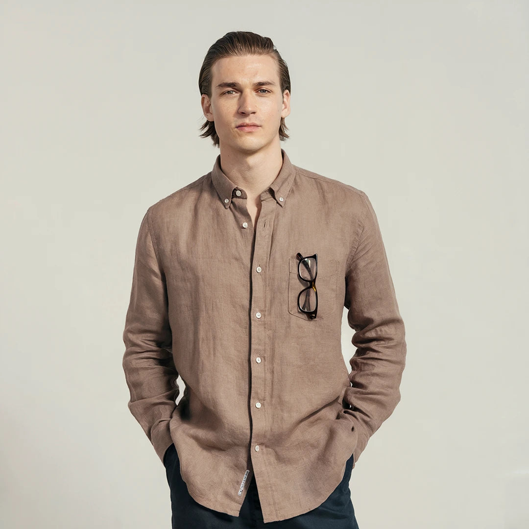 A man wearing a brown linen shirt with a classic spread collar and mother-of-pearl buttons, paired with dark trousers.