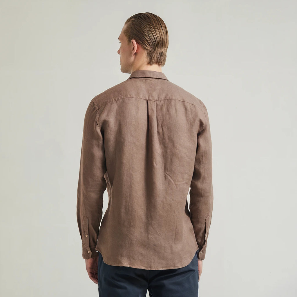 A man wearing a brown linen shirt with a classic spread collar and mother-of-pearl buttons, paired with dark trousers.