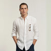 A man wearing a white linen shirt with a classic spread collar and mother-of-pearl buttons, paired with dark trousers.